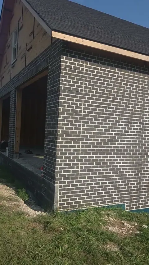 Dark brick veneer turning the corner of a new house above a block foundation.